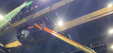 Service technician on a lift installing new hoist motor on crane runway 56 feet in the air.